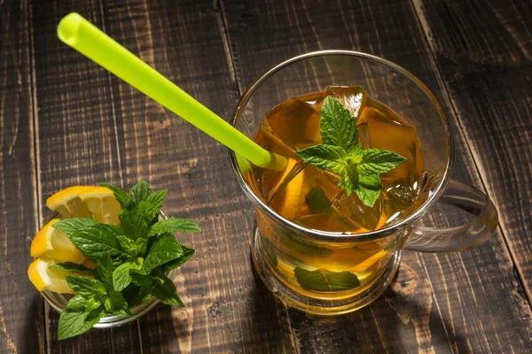 tea with ice and mint in a glass cup on wooden boards, near mint and lemon