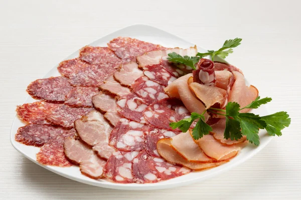 There is a variety of sausages and prosciutto on the plate, the meat assortment is decorated with parsley