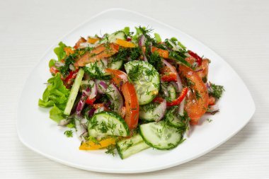 Taze salatalık, domates ve soğan salatası, yeşilliklerle süslenmiş, beyaz bir tabakta.