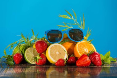 Yaz konsepti, nane ve tarhun ile çevrili çilek, portakal ve limon dağı, ıslak tahta tahtalar, mavi arka plan