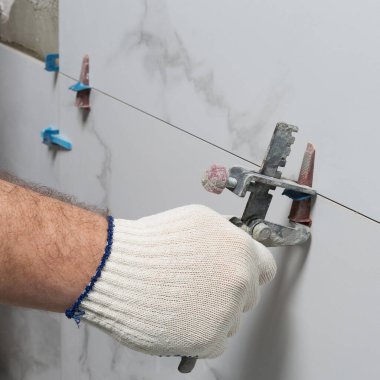 Usta elinde bir alet tutuyor, seramik fayanslar arasındaki boşluğu kontrol ediyor, banyo odasına fayanslar yerleştiriyor, odayı onarıyor.