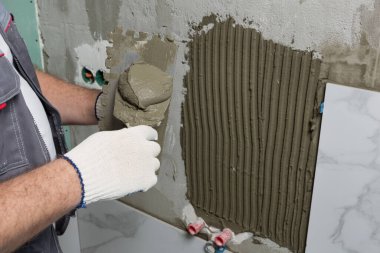 Ustanın elleri duvara seramik fayanslar için yapışkan bir solüsyon uygular, banyoya fayanslar serer, odayı yeniler.