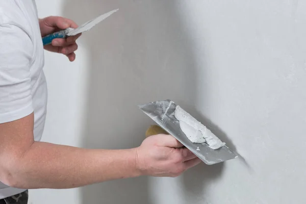 Usta elinde havan topu olan bir spatula tutuyor, duvara dekoratif alçı yapıştırıyor, binayı onarıyor.