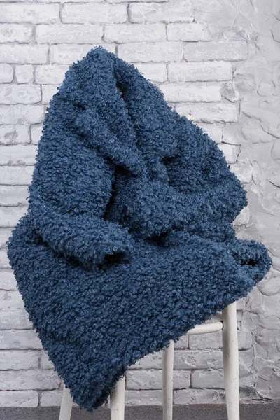Blue eco fur coat, faux fur, thrown on a chair, against a brick wall, concept