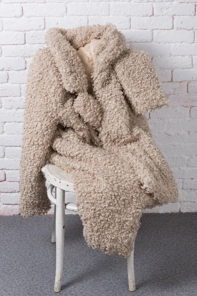 Beige fashionable faux fur coat as if sitting on a chair against a white brick wall, concept