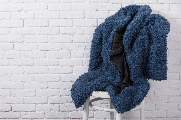 Blue eco-friendly faux fur coat, as if sitting on a chair against a white brick wall, copy space