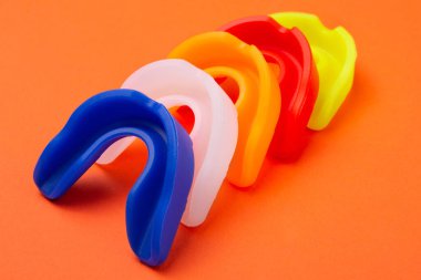 Beş renkli boks ağız koruyucusu, yan yana, turuncu arka planda, köşegen pozisyonda.