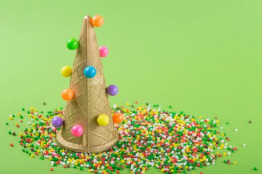 çok renkli tatlılar yeşil bir arka plana saçılmış, yanında bir dondurma külahı çok renkli toplarla süslenmiş, konsept