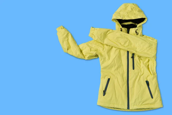 yellow women\'s winter ski jacket from raincoat fabric, on a blue background, concept, copy space
