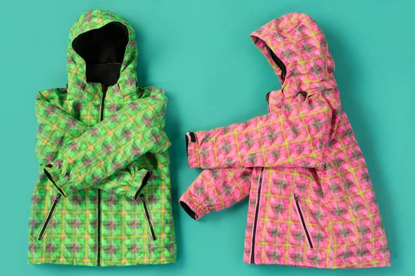 two ski jackets lie as if the sleeves are showing gestures, concept, on a turquoise background