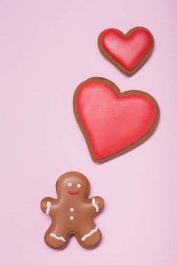 gingerbread man and two gingerbread in the form of a red heart on a pink pastel background, the idea of a minimal concept