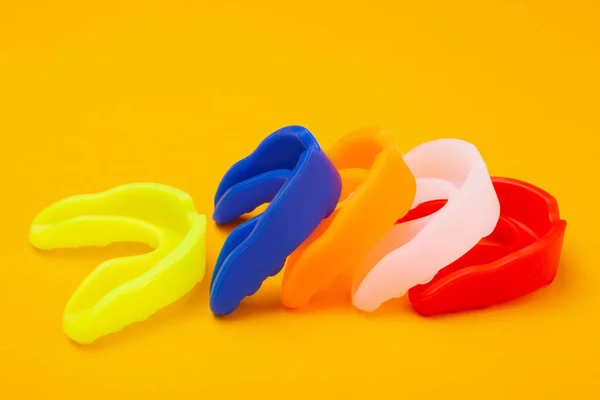 five colored boxing mouth guards laid out in a row on a yellow background, concept, horizontal layout