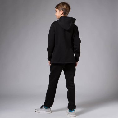 Siyah eşofmanlı genç bir çocuk, tam büyümüş, gri bir arka planda, sırtını döndü.