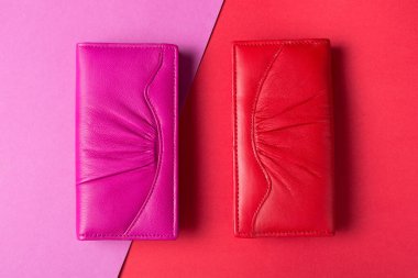 İki kadın deri cüzdanı, kırmızı ve pembe. Renkli arka planda, pembe ve kırmızı, düz yerde.