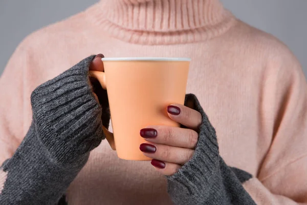In female hands with long sleeves of a woolen sweater a cup with a hot drink, the concept of warmth and comfort, selective focus