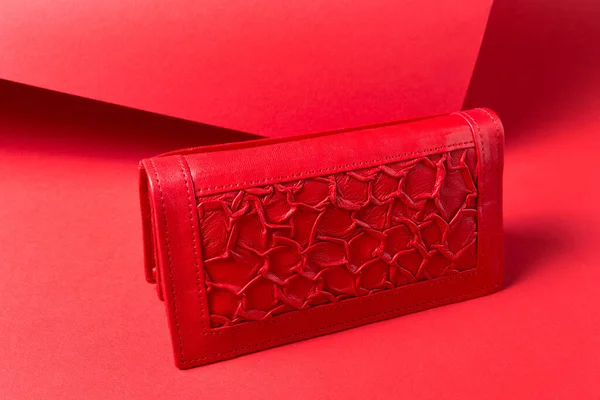 Red women\'s leather wallet with a textured finish, located on a red background, concept