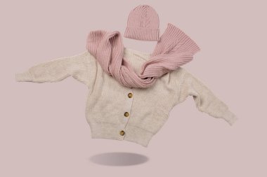 Düğmeli bej kazak, pembe atkı ve şapka, sanki havada asılı, pembe arka planda bir gölge, bir konsept,