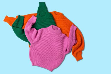 Üç örgü süveter, pembe, yeşil ve turuncu, birbirinin üstüne konsept konsept, arka planda rastgele atılmış.