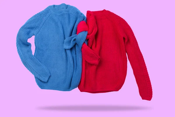 Two knitted sweaters, blue and red, are intertwined with sleeves, like a couple of people, levitation, concept, on a lilac background
