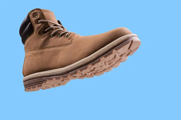brown high boot, as if hanging in the air, bottom view, concept, winter shoes for an active lifestyle, on a blue background, copy space