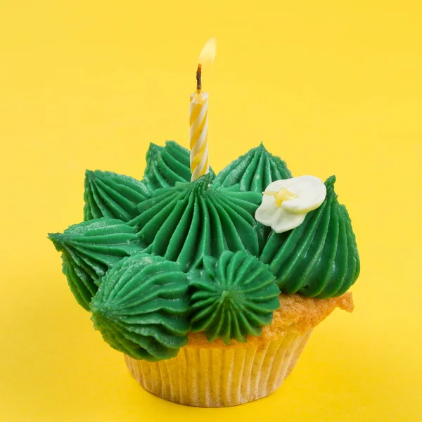 サボテンの形をした緑色のクリームとカップケーキ 燃えるキャンドル 黄色の背景に 誕生日の概念 — ストック写真
