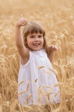 Buğday tarlasında mutlu bir çocuk, gülüyor ve olumlu bir jest yapıyor, olgunlaşmış sarı buğday, kavram