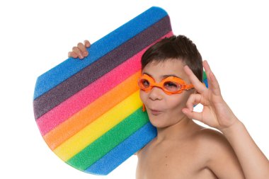 Turuncu gözlüklü mutlu bir sporcu elinde çok renkli bir yüzme tahtası tutuyor ve jest yapıyor.