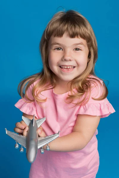 ピンクのドレスを着た幸せな女の子は飛行機を手に持ち笑い旅行の夢休暇のコンセプト青い背景 — ストック写真