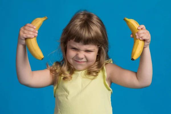 黄色の二つのバナナを持つ黄色のブラウスの女の子は 手が持ち上げられます コンセプト 青の背景に — ストック写真