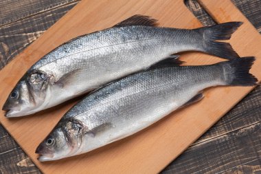 Tahta kesme tahtasının üzerinde iki balık uzanıyor. Taze deniz balığı, levrek, dümdüz uzanmış.