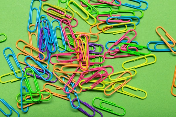 a lot of multicolored paper clips scattered on a green background, flat lay