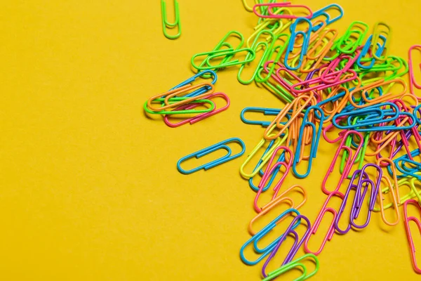 a lot of multicolored paper clips scattered on a yellow background, office concept, copy space