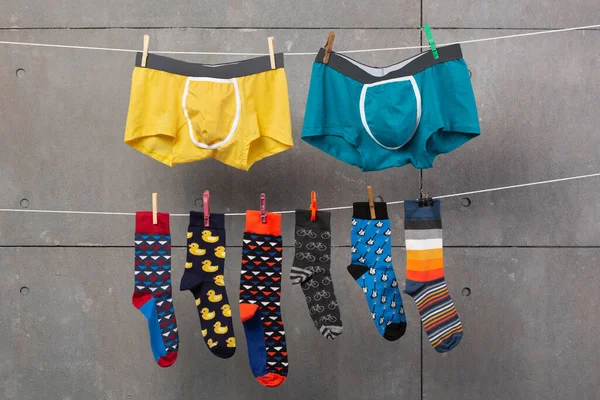 2人の男性のショートパンツと多くの色の靴下がロープにかかっています洗濯後に乾燥するかのように コンセプトは 灰色のグランジの背景に ロイヤリティフリーのストック画像