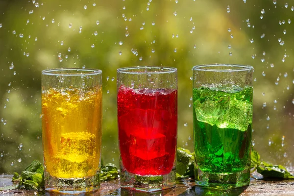 Tre Glas Med Färgade Drycker Och Isbitar Träskiva Mot Bakgrund — Stockfoto