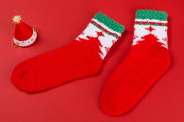Kırmızı arka planda, Noel ağacının yanında yürüyormuş gibi iki kırmızı Noel çorabı.