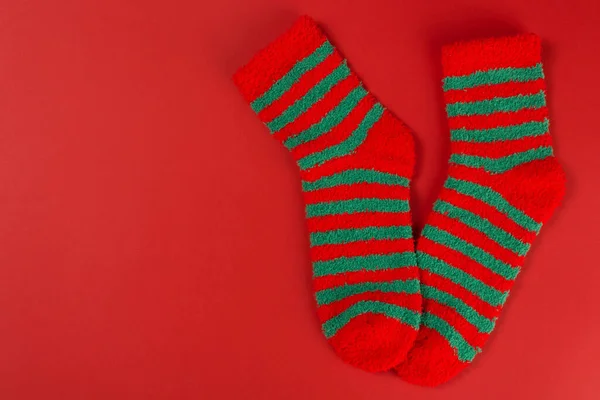 Two green striped Christmas socks, as if standing on toes, on a red background, concept, flat lay