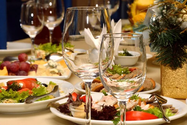 Farklı yemek ve içeceklerle dolu bir şölen masası. Boş cam bardaklar. Tabaklar yiyecekle dolu..