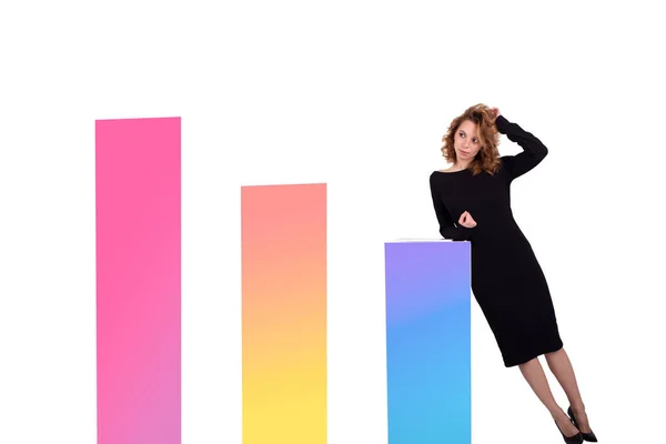 Beyaz arka plandaki renkli diyagramların yanında siyah elbiseli çekici beyaz iş kadını.
