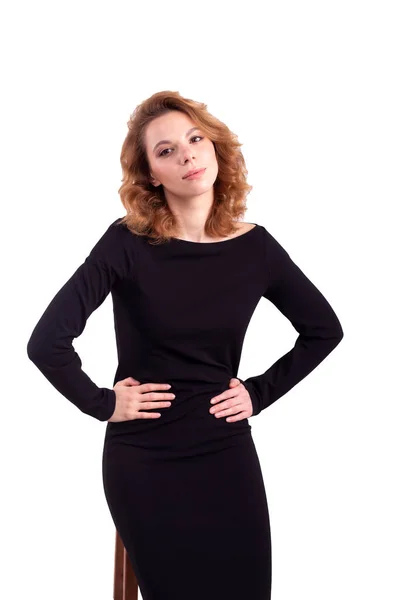 Siyah elbiseli, elleri kalçasında beyaz arka planda şüpheli bir bakışla genç bir kadın.