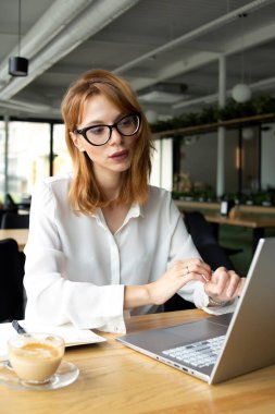 Business woman in public place in white shirt sitting at the table with laptop and smiling