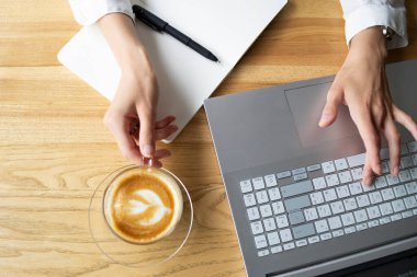 Closed up cup of coffee in a transparent cup with a hand and laptop on the background