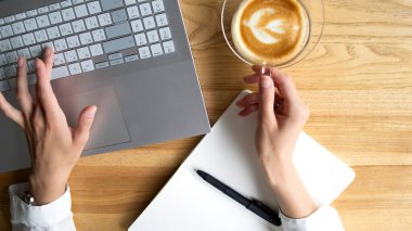 Beautiful hands in a white shirt with a cup of coffee laptop and notebook