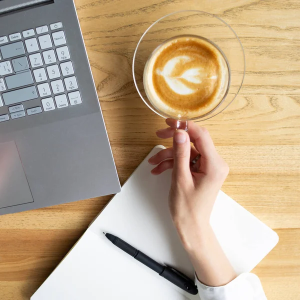 Kahve ve dizüstü bilgisayarın kapağı ahşap masada, güzel bir elle.