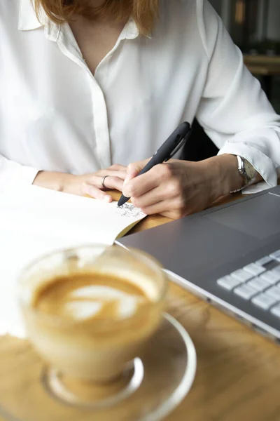 Güzel iş kadınlarının elleri dizüstü bilgisayarın yanında notlar alıyor.