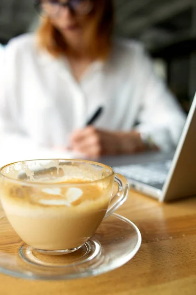 Ön planda beyaz gömlekli bir iş kadını olan şeffaf kahve kapuçinosu.