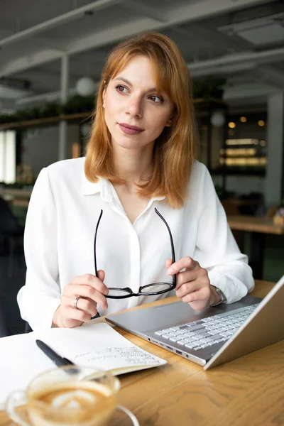 Masadaki iş kadını halka açık bir yerde dizüstü bilgisayarla beyaz gömlek giyiyor.