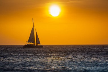Idyllic caribbean beach with sailboat in Aruba at golden sunset, Dutch Antilles