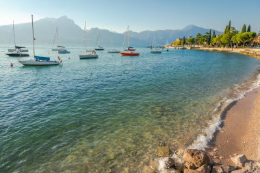 Idyllic lake Garda coastline in Castelletto with sailboats and mountains, Northern Italy
