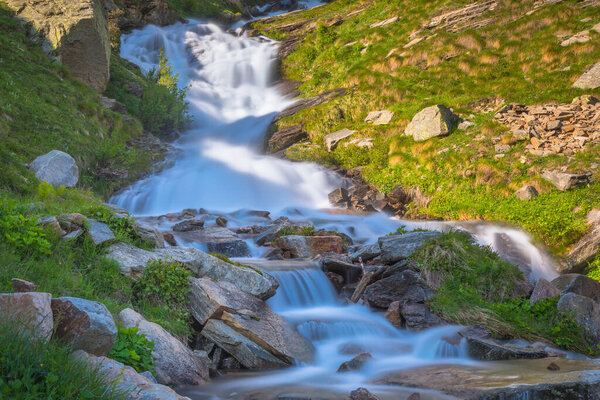 Ethereal waterfall and alpine meadows at springtime, Gran Paradiso Alps, Italy, border with France