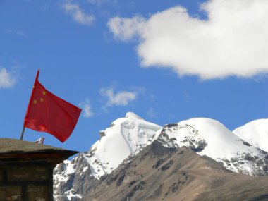 Tibet 'te derin mavi gökyüzünün altında kar kaplı dağların önünde Çin ulusal bayrağı